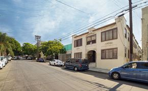 Los Angeles apartment for rent - A street view with cars parked on the side of the road and a building with a blue awning in the background.