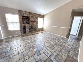 Hesperia house for rent - A stone fireplace is in the corner of a room with tile flooring.