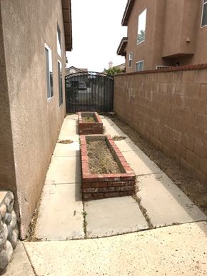 Hesperia house for rent - A long concrete walkway leads to a brick planter box.