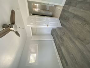 Ontario triplex for rent - A ceiling fan is mounted on the wall above a window in a room with wood flooring.