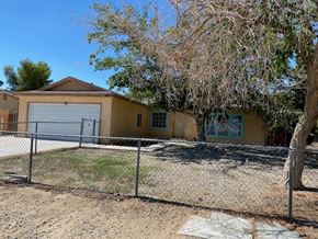 Adelanto house for rent - A yellow house with a grey garage door and a fence.