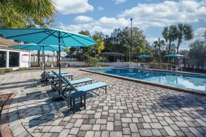 Jacksonville apartment for rent - A pool area with a blue umbrella and a brick patio. at Red Bay Apartment Complex, Jacksonville, FL, 32211