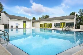 Jacksonville apartment for rent - A swimming pool in front of a white building with yellow doors.