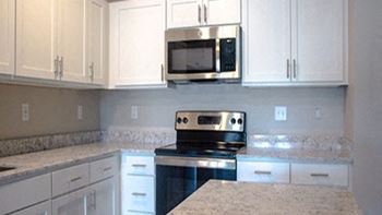 A kitchen with white cabinets and a stove and a microwave