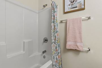 Eugene townhouse for rent - A white bathtub with a floral shower curtain and a pink towel hanging on a towel rack.
