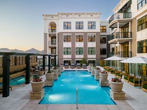 Phoenix apartment for rent - A large swimming pool is surrounded by potted plants and lounge chairs.