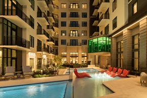 Dallas apartment for rent - A modern apartment complex with a pool and lounge chairs.