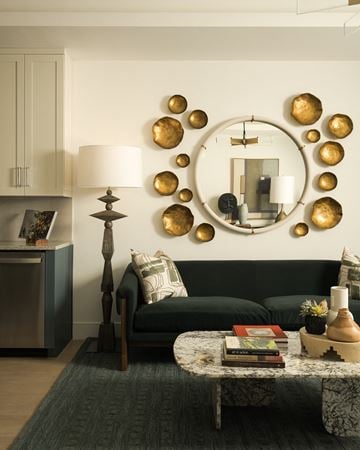 Scottsdale apartment for rent - A living room with a black couch, a round mirror with gold circles, and a table with a lamp and a plant.