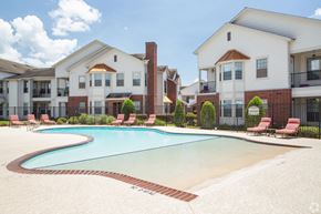 Zachary apartment for rent - A swimming pool surrounded by red chairs and buildings.