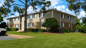 Perry apartment for rent - A building with a brown and beige exterior is surrounded by a green lawn and trees.