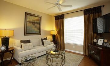 Houma apartment for rent - A living room with a white couch, a painting on the wall, a ceiling fan, and a glass coffee table.