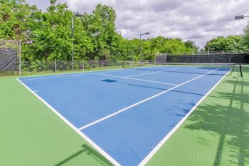 Blue tennis court surrounded by trees and fencing