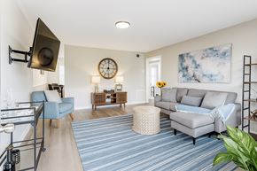 Jacksonville apartment for rent - A living room with a grey couch, a blue chair, and a clock on the wall.