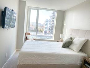 Vancouver condo for rent - A bedroom with a large bed and a flat screen TV mounted on the wall.
