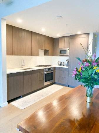 Vancouver condo for rent - A kitchen with wooden cabinets and a wooden table with a vase of flowers on it.