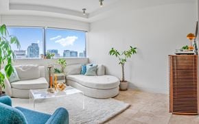 Vancouver apartment for rent - A living room with a white couch, a glass table, and a large window with a view of the city.