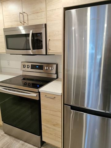 Vancouver apartment for rent - A stainless steel refrigerator stands next to a stove and microwave in a modern kitchen.