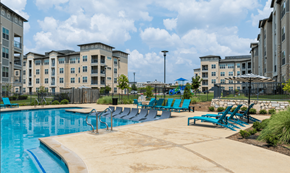 Round Rock apartment for rent - A swimming pool surrounded by blue lounge chairs and buildings in the background.
