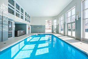 Sainte Therese apartment for rent - Bourg du Village indoor pool with high ceilings and floor to ceiling windows and patio door leading to outdoor patio area in Sainte Therese, QC