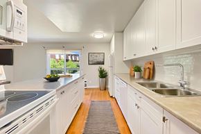 Belleville apartment for rent - A modern, partially-open, galley style kitchen with white cabinets and a grey countertop at Moira Apartments in Belleville, ON