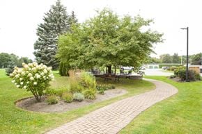 Barrie apartment for rent - Sunnidale Place garden area with bench seating and patio in background in Barrie, ON