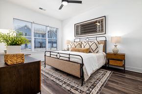 Wake Forest apartment for rent - A bedroom with a large bed, a wooden nightstand, and a plant on a table.
