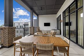 Wake Forest apartment for rent - A wooden table with chairs is on a patio with a brick pillar and a glass door.