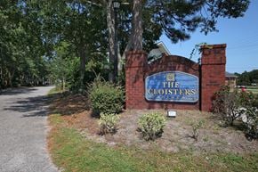 Myrtle Beach apartment for rent - The entrance to The Cloisters with a blue sign on a brick wall. The Cloisters Apartments, 902 67th Avenue North, Myrtle Beach, SC