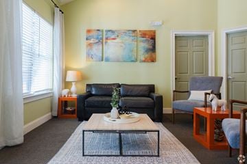 Dallas apartment for rent - A living room with a grey couch, a blue chair, and a painting on the wall.