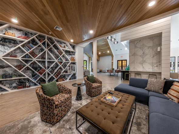 Austin apartment for rent - A community lounge in The Shiloh's clubhouse with comfortable seating near a wall with modern geometrical shelving.