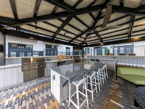 Austin apartment for rent - An outdoor kitchen under a covered patio with two barbecue grills, a sink, granite countertops, a ceiling fan, and an island with barstools near a lounge area.