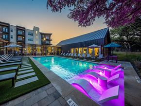 Austin apartment for rent - A resort-style pool surrounded by lounge chairs and umbrellas near a community gym and apartment buildings.