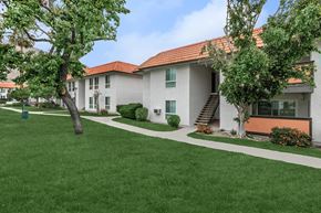 Palm Springs apartment for rent - A white building with a red roof is surrounded by a green lawn.