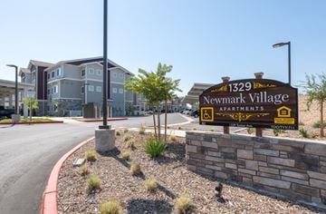 Sanger apartment for rent - A sign for Newmark Village Apartments is in front of a building.