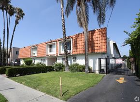 Reseda apartment for rent - A white house with a red tile roof is surrounded by palm trees.