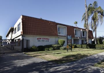 Reseda apartment for rent - A building with a sign that says "NOW LEASING!" is surrounded by a fence and palm trees.