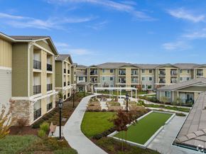 Gilroy apartment for rent - an exterior view of an apartment complex with a green courtyard