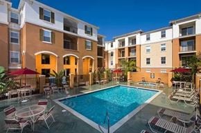 Buena Park apartment for rent - A swimming pool surrounded by chairs and umbrellas in front of apartment buildings.