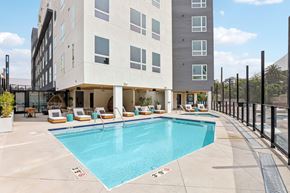 Los Angeles apartment for rent - A large swimming pool is surrounded by lounge chairs and a building.