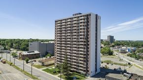 Ottawa apartment for rent - A tall building with many windows is surrounded by a parking lot.