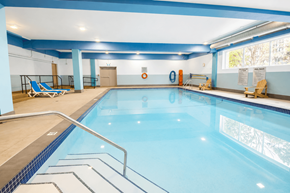 Gatineau apartment for rent - A large indoor swimming pool with a blue tiled edge and a metal ladder.