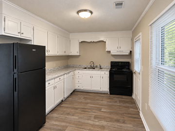 Clemson apartment for rent - A black refrigerator stands in a kitchen with white cabinets and a wooden floor.