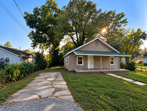 Anderson house for rent - A house with a green roof is surrounded by trees and has a driveway leading to the front door.