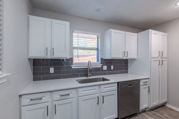 Euless townhouse for rent - A kitchen with white cabinets and a grey backsplash.