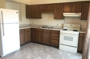 Elysburg apartment for rent - A white refrigerator stands in a kitchen with wooden cabinets and a white stove.