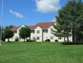 Mcveytown apartment for rent - A white building with a brown roof is surrounded by a green lawn.