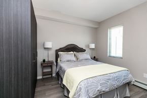 Calgary apartment for rent - A bedroom with a large bed and a nightstand with a lamp.