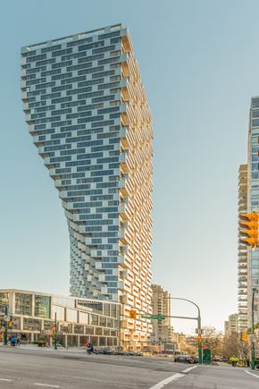 Vancouver condo for rent - A tall, modern building with a curved glass facade stands in the foreground of a city street.