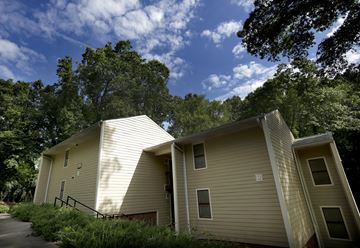 Charlotte apartment for rent - A beige house with a sloped roof is surrounded by trees.