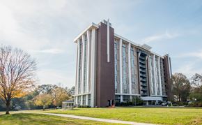 Charlotte apartment for rent - A large, modern building with a red and white facade stands in a grassy area with trees in the background.